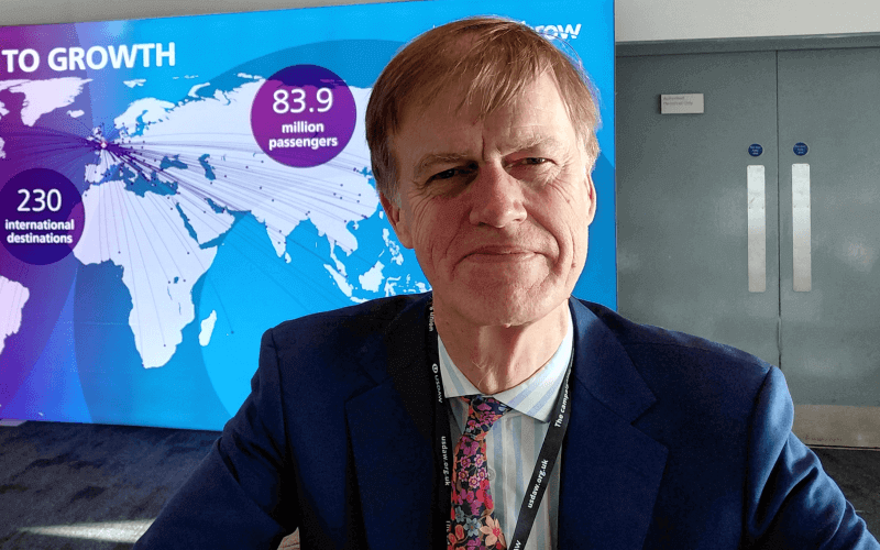 Stephen Timms head and shoulders in a suit and tie, smiling, with a map of the world in the background