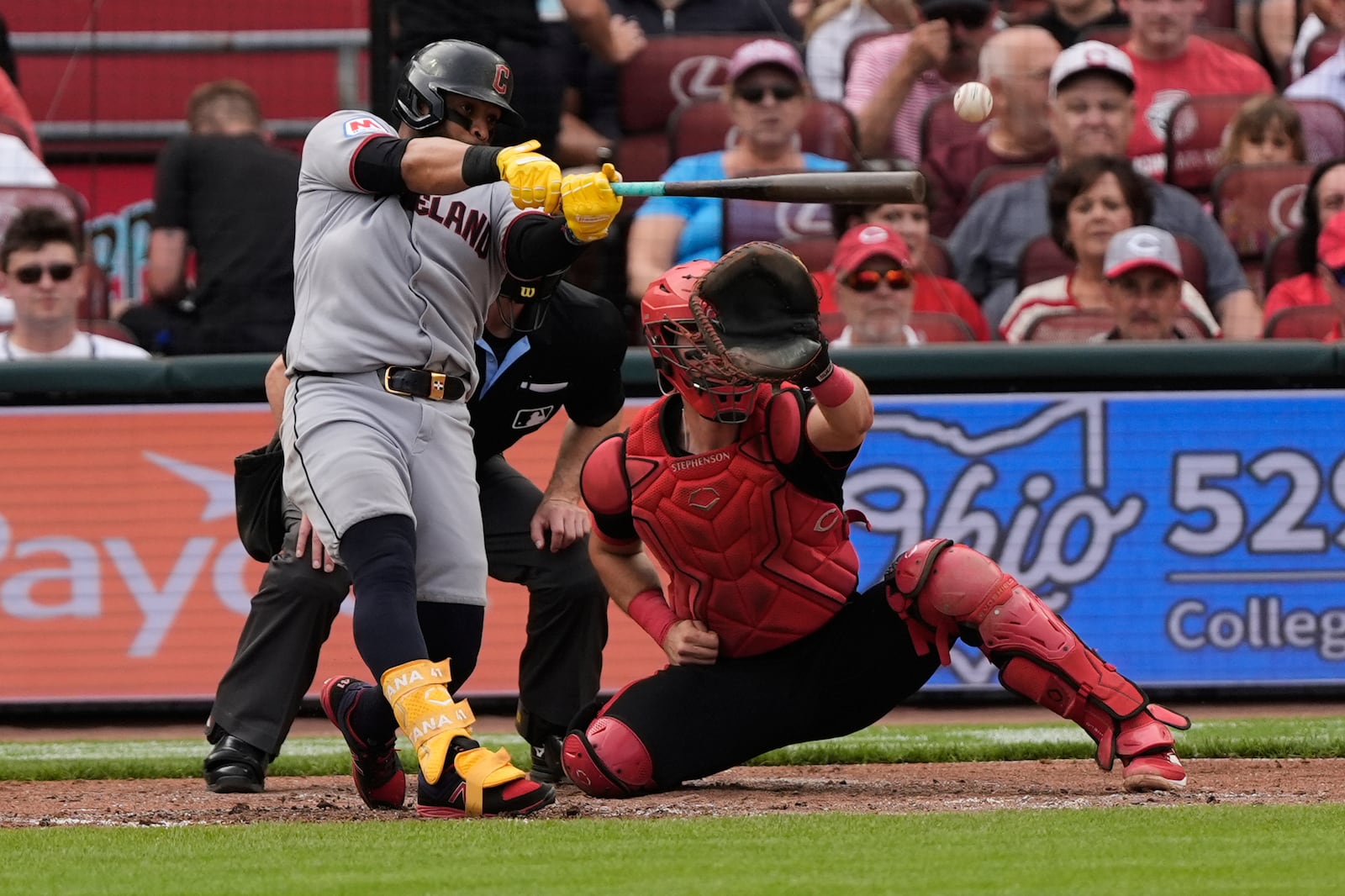 Cleveland Guardians' Carlos Santana, left, hits a single to score Steven Kwan and Kyle Manzardo as Cincinnati Reds catcher Tyler Stephenson, right, and home plate umpire Ben May, center, look on during the fourth inning of a baseball game, Friday, May 16, 2025, in Cincinnati. (AP Photo/Carolyn Kaster)