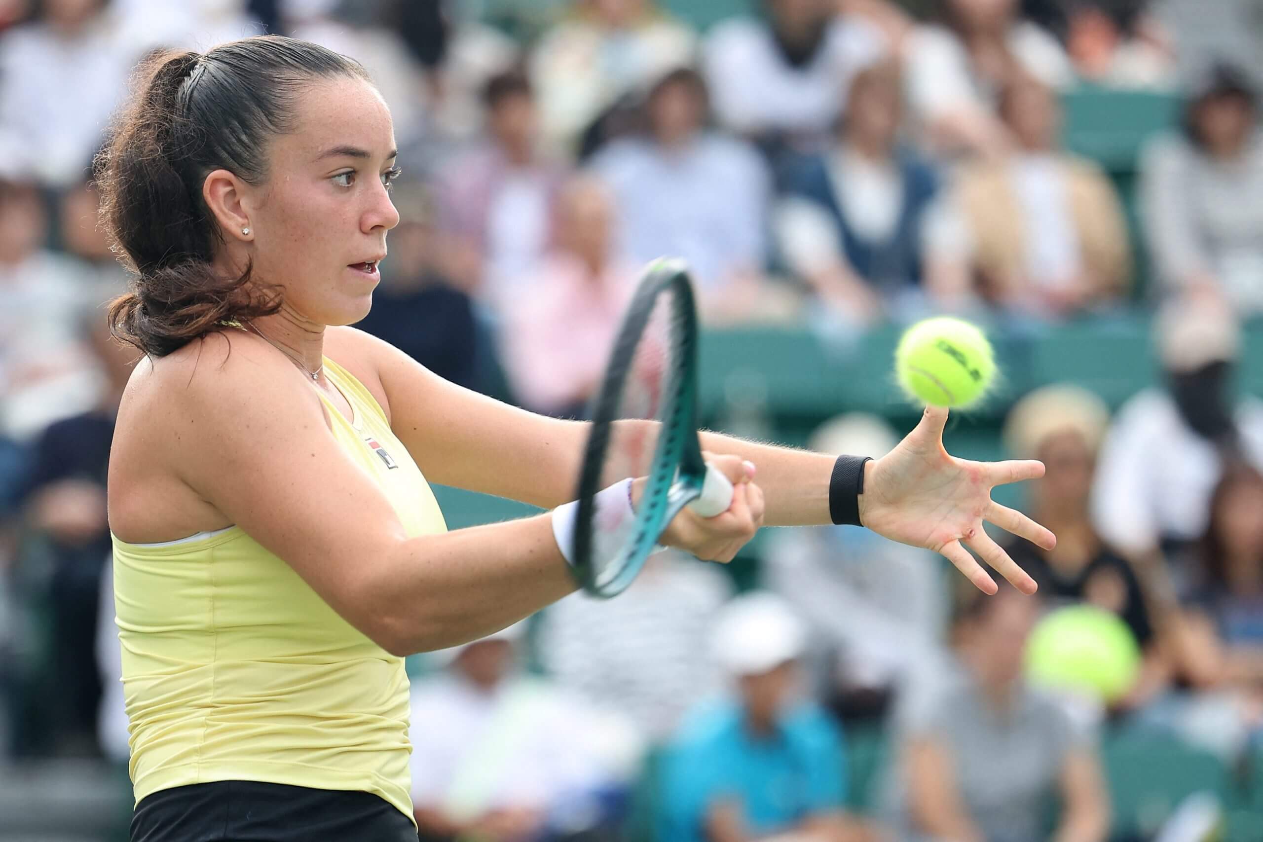 Tennis player Tereza Valentová prepares to hit a forehand, with fans in the stands in soft focus in the background.