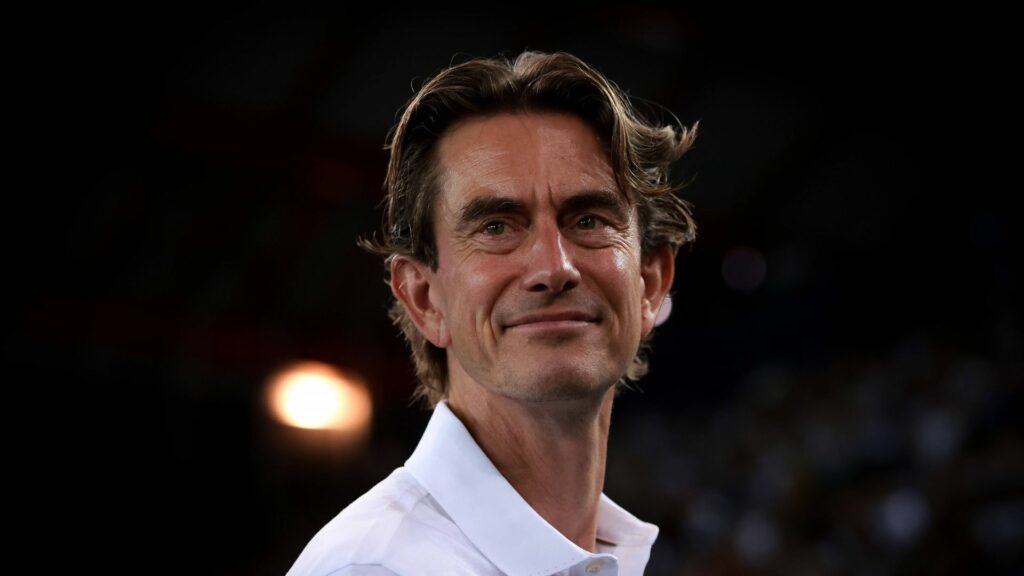Tottenham manager Thomas Frank smiles in front of a dark background.
