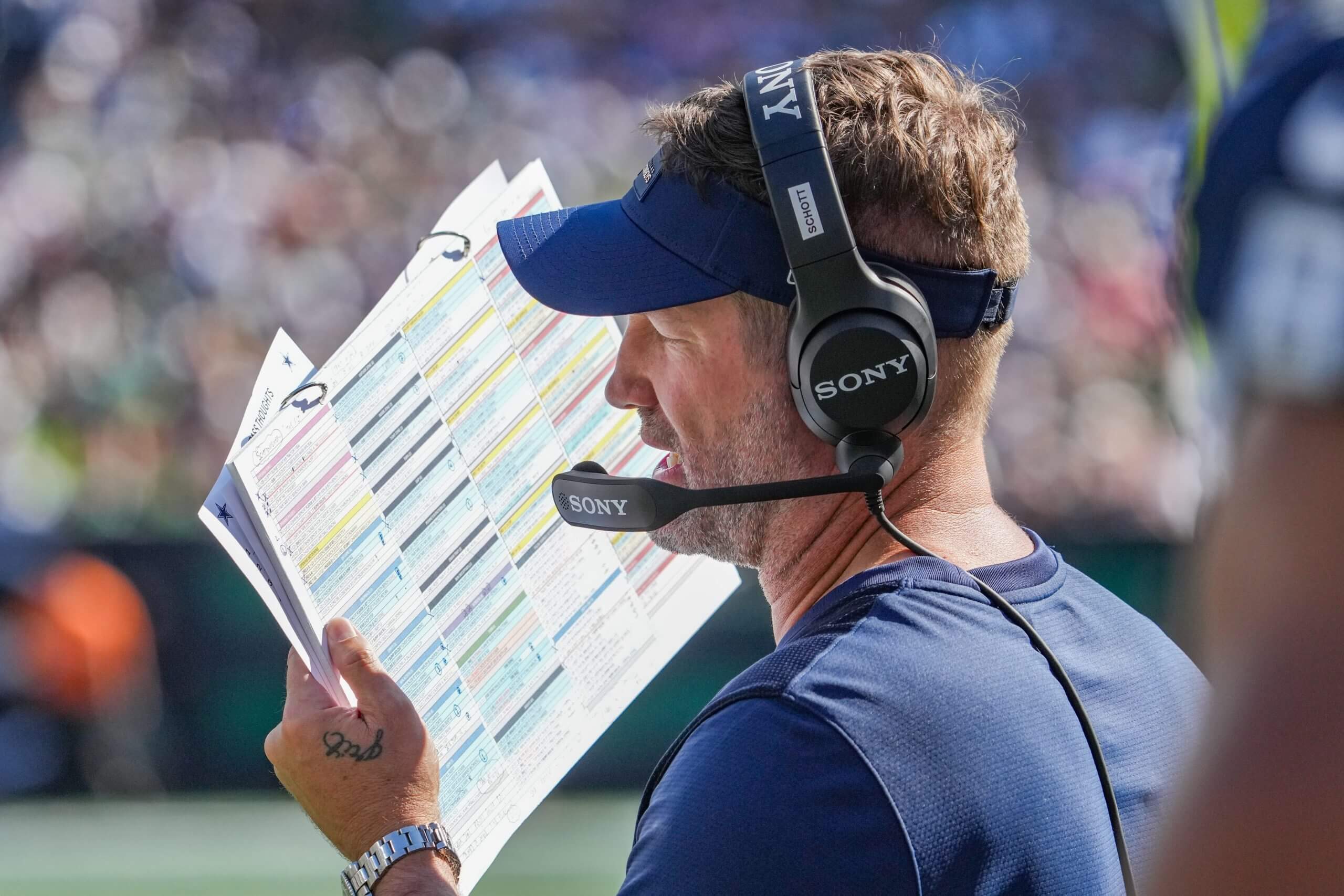 Dallas Cowboys coach Brian Schottenheimer looks at his play sheet as he speaks into his headset.