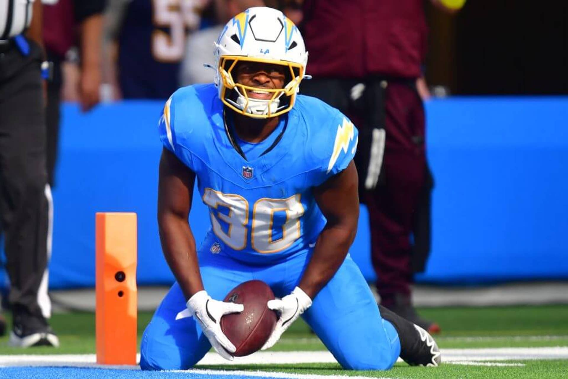 Kimani Vidal on his knees with a football in his hands near the end zone wearing the blue L.A. Chargers uniform.