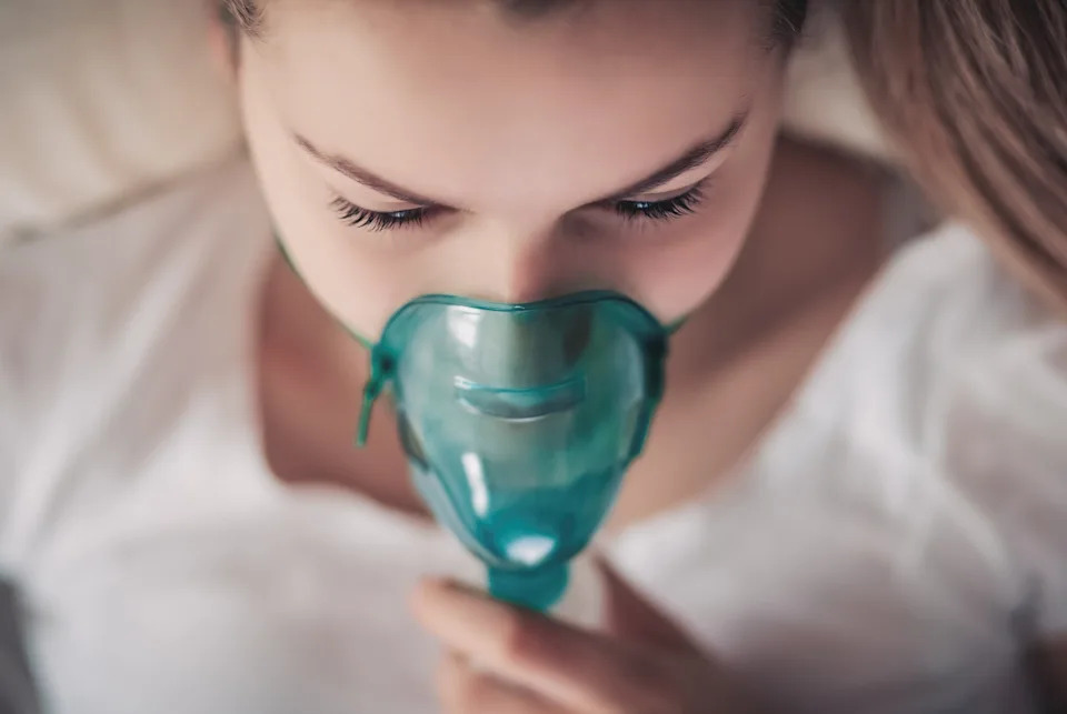 A person lying down uses a medical oxygen mask, appearing serene and relaxed