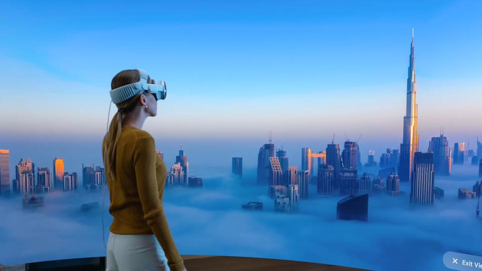 A person wearing Apple's Vision Pro headset looks at a virtual panorama of a city in clouds.