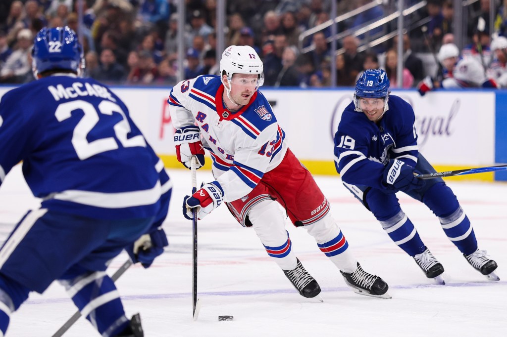 Alexis Lafrenière of the New York Rangers skates with the puck, flanked by two Toronto Maple Leafs players.