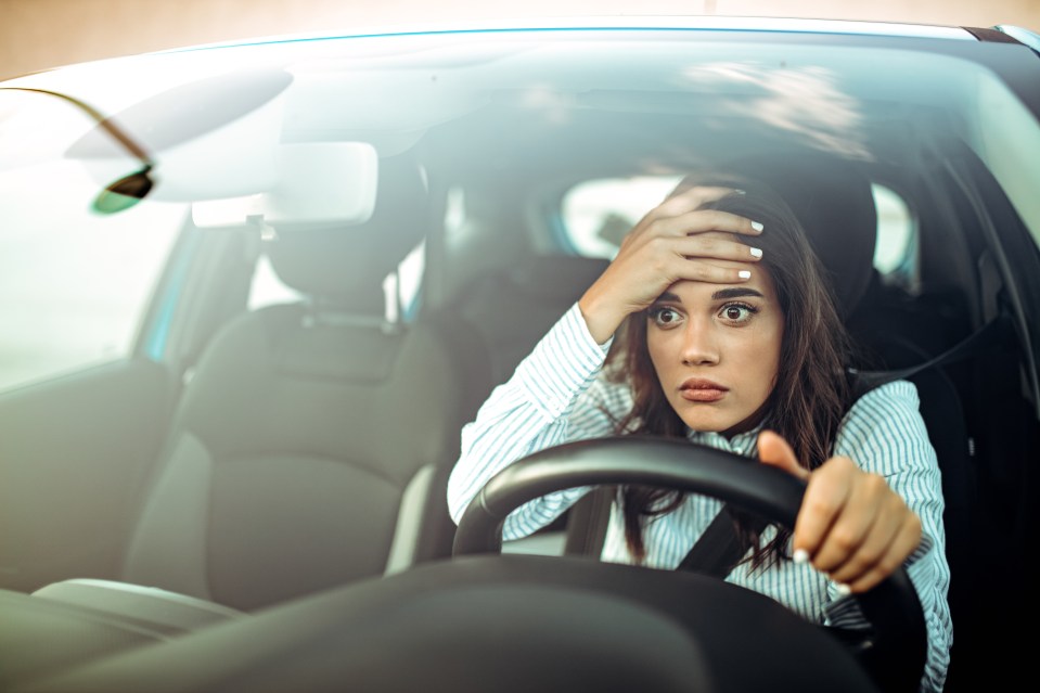 Frustrated woman with her hand on her forehead while driving a car.