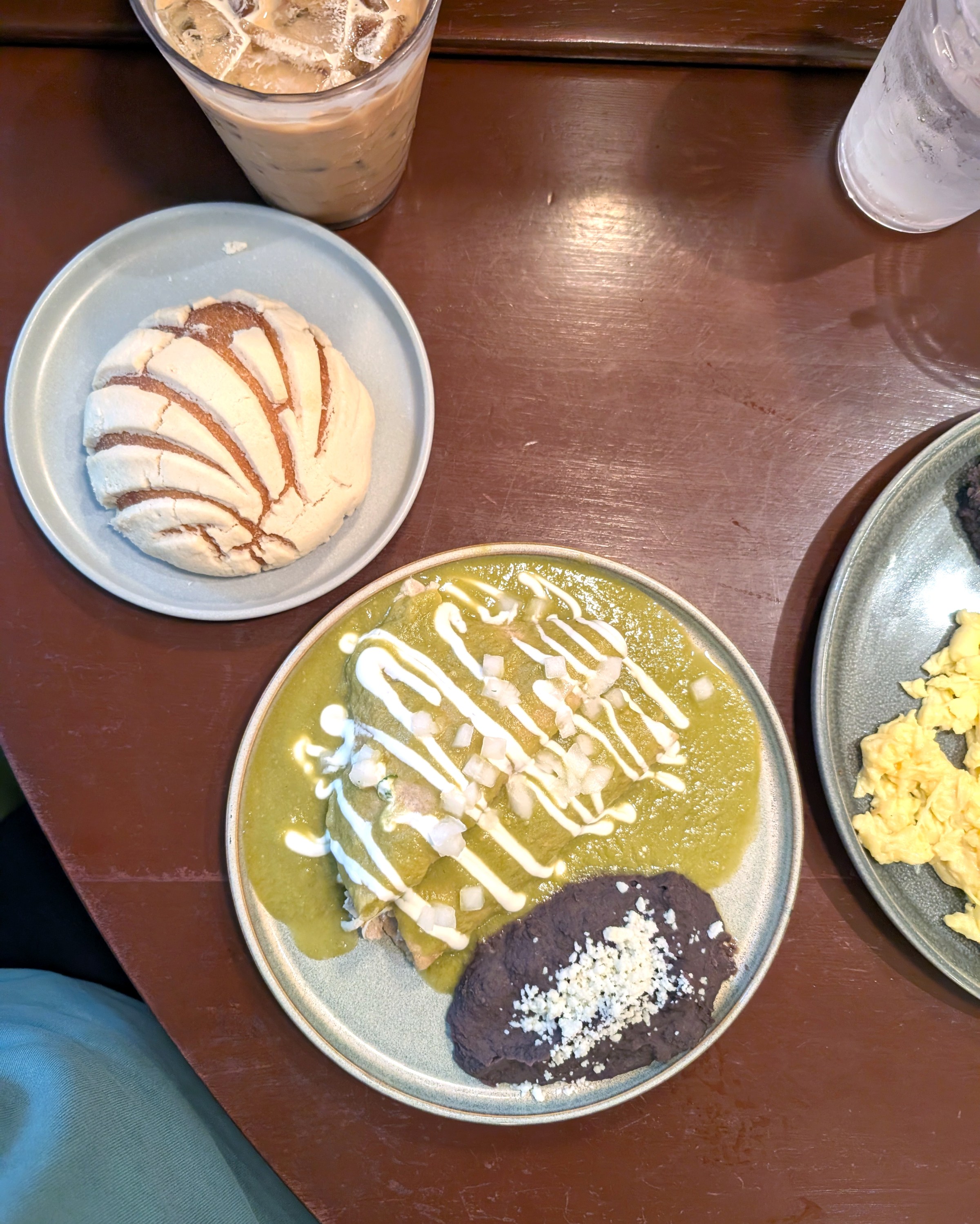 A plate of green sauce with white sauce squiggles next to a dark brown sauced item on a plate next to a baked bread on a different plate.