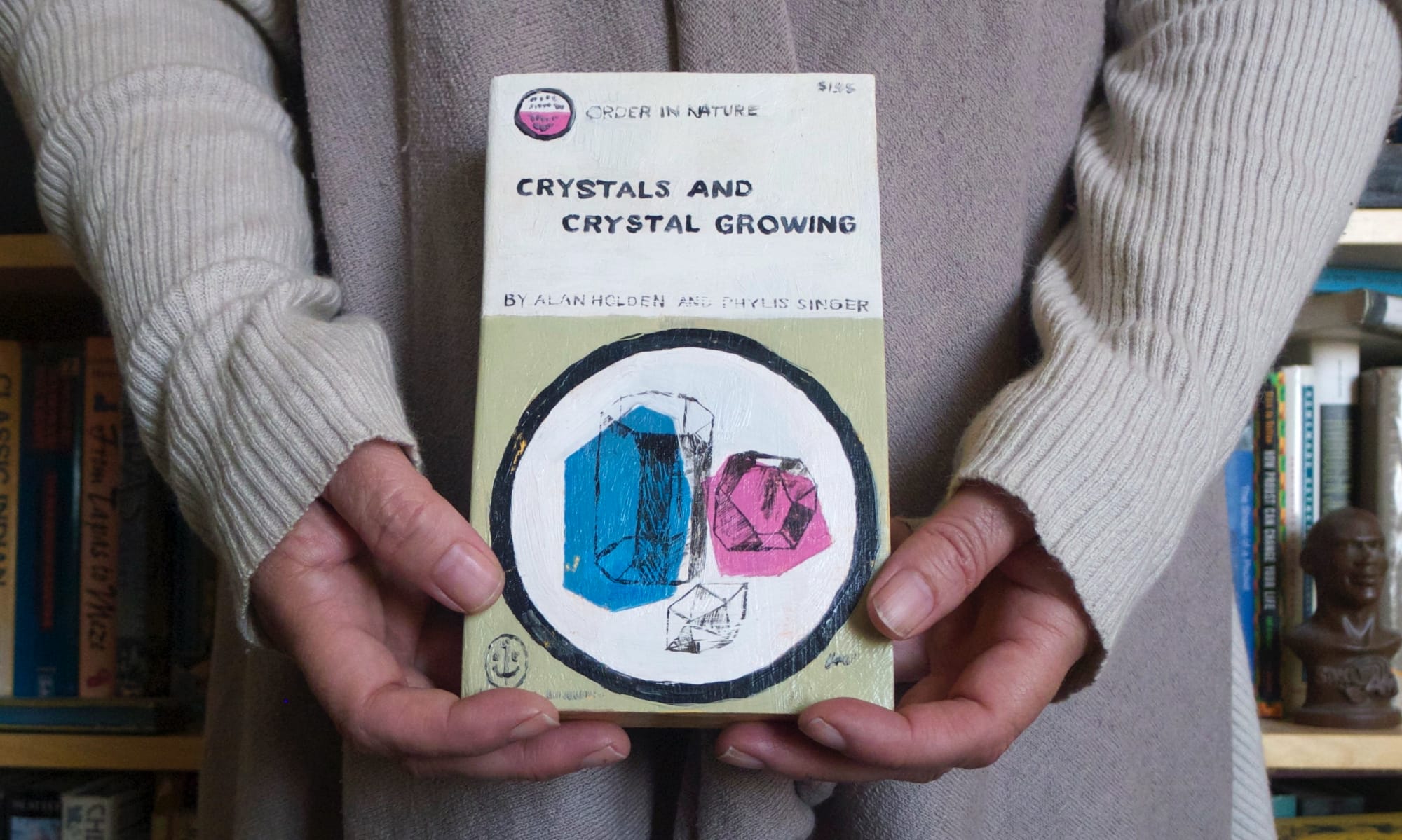 Conrad Bakker's wooden sculpture of a book called "Crystals and crystal growing" photographed while held in a person's hands