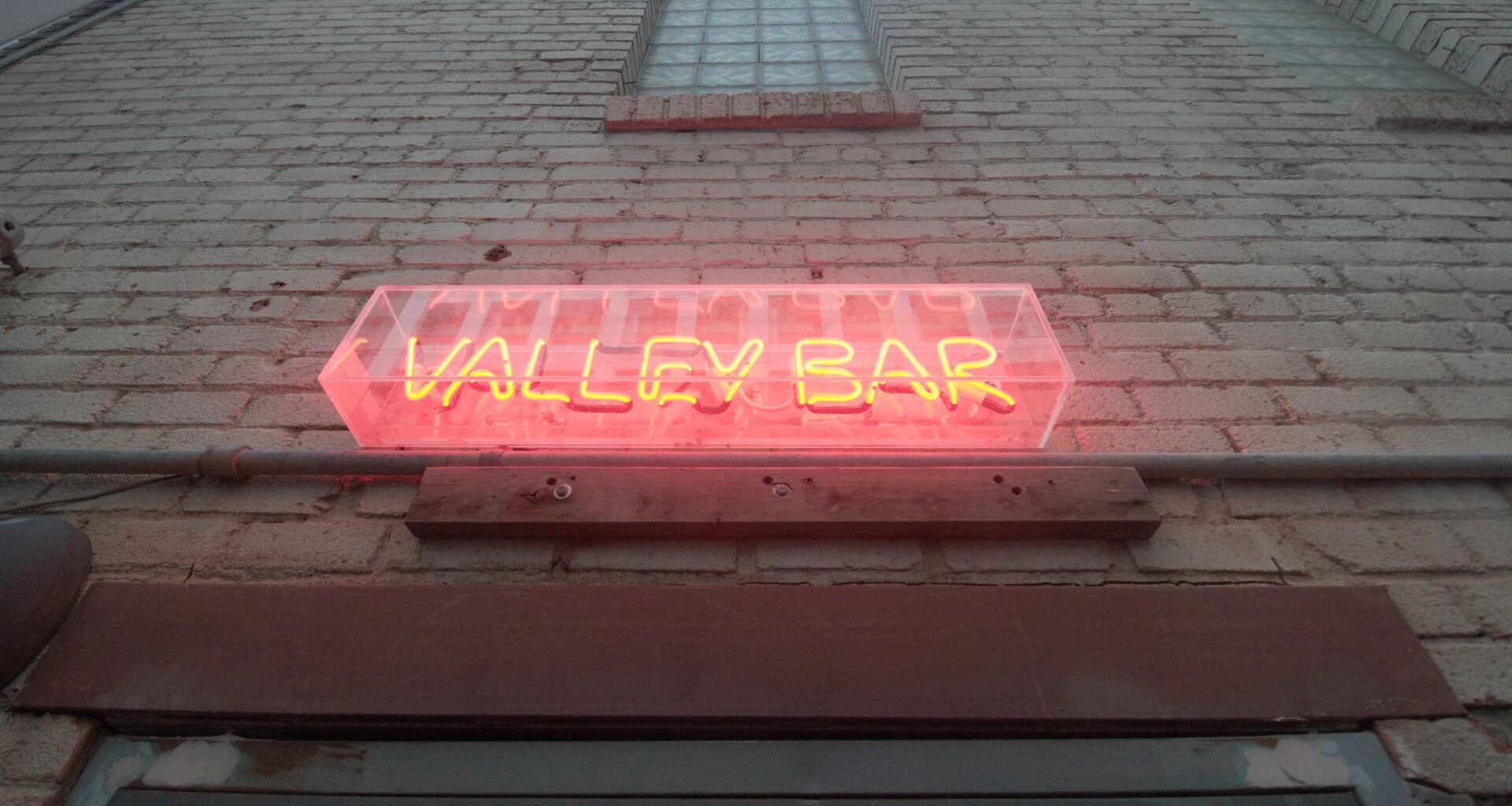 A neon sign on a brick wall above a door.