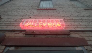 A neon sign on a brick wall above a door.
