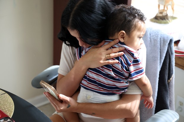 Mom holds her son Lennyel, age 1, on Sept. 23, 2025, while talking to her husband, Darwin Leal by phone.(Terrence Antonio James/Chicago Tribune)