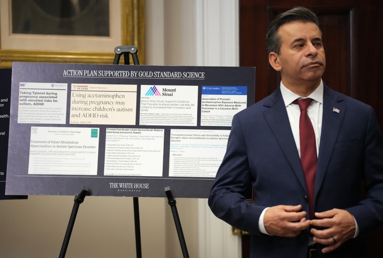 Marty Makary standing next to an easel which holds a board with "Action plan supported by gold standard science" printed on the top, and clippings showing titles of research papers pasted below
