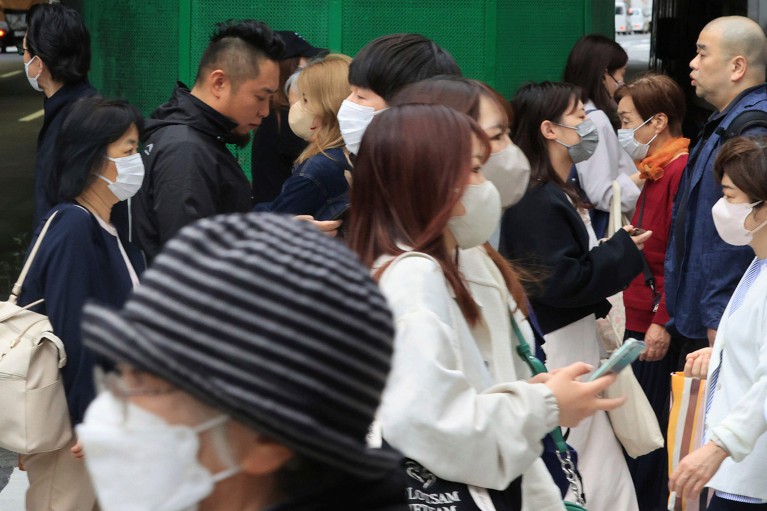 A crowd of mask wearing commuters on a busy street in Osaka City.
