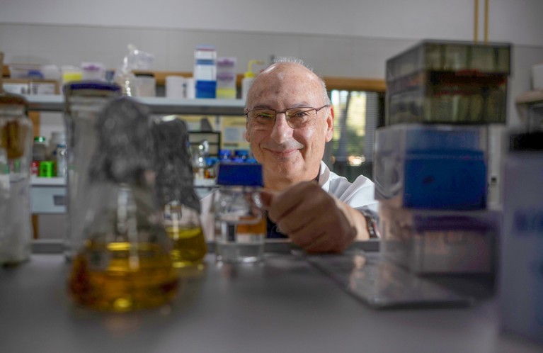 Portrait of Francisco Mojica viewed through a shelf in a laboratory filled with flasks and bottles.