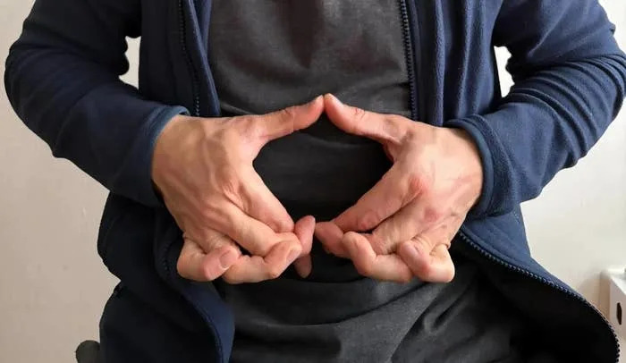 Person seated, hands forming a heart shape over abdomen, suggesting a focus on health, mindfulness, or self-care