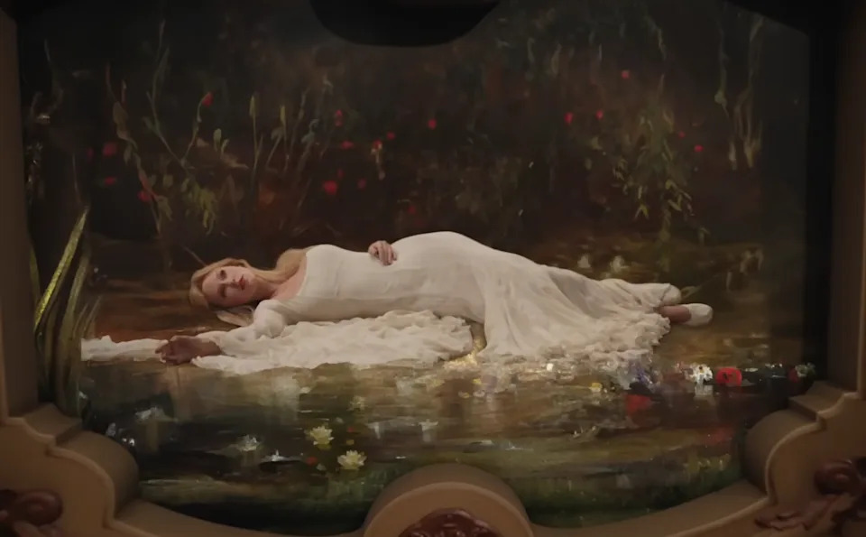 Person in a flowing white dress lies on a painted backdrop resembling a serene natural setting with flowers