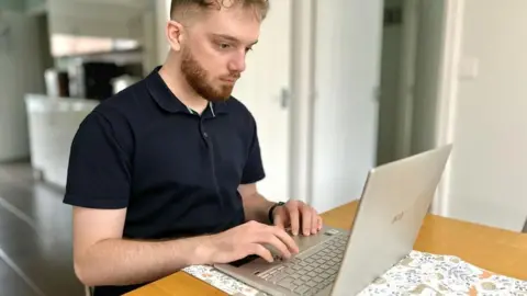 Martin Giles/BBC Joe Burgess on his lap top computer in his Felixstowe home looking for jobs