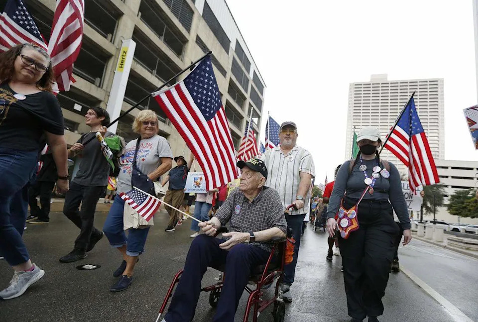 Ninety-five-year-old Korean War veteran William Johnson, center, and others march through downtown streets during the No Kings protest in Fort Worth on Saturday, Oct. 18, 2025.