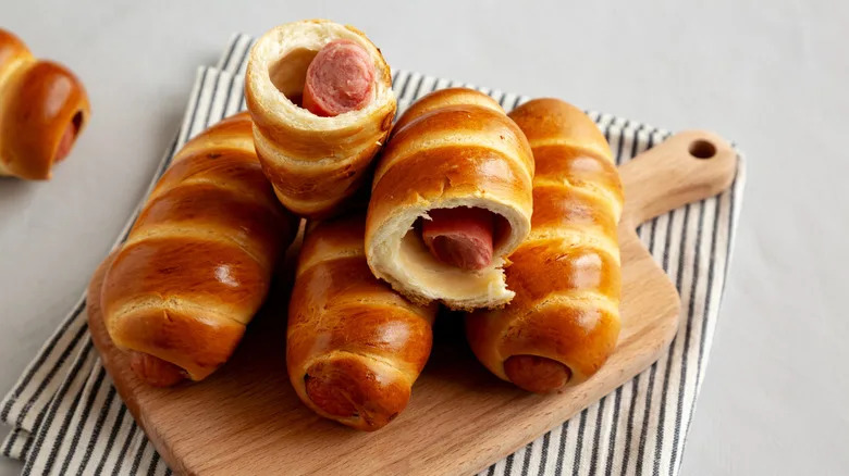 Traditional Czech sausage pastries on a wooden tray with a striped cloth underneath