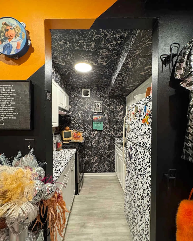 Narrow kitchen with black and white patterned walls, white cabinets, and colorful decor, including a vintage microwave.