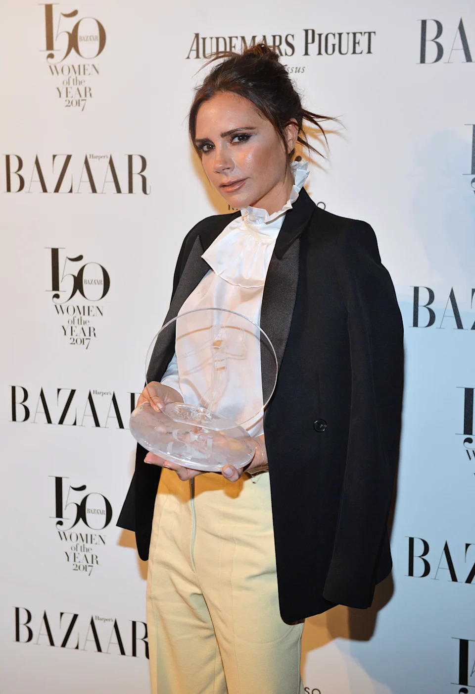 Victoria holds the British Brand of the Year award as she poses in front of a Harper's Bazaar backdrop.