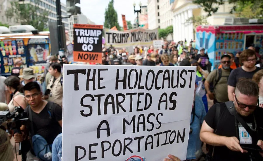 Demonstrators hold a sign “The Holocaust started as mass deportation” during the “No Kings” protest at Lafayette Square in Washington, DC, on June 14, 2025, the day of President Trump’s military parade. In response to the military parade celebrating the 250th anniversary of the US Army but also coinciding with Trump’s 79th birthday, a “No Kings” movement has sprung up promising to stage protests in more than 2,000 places across the country, including a large parade expected in Los Angeles which organizers say will feature a “20-foot-tall balloon of Trump wearing a diaper.” (Photo by Amid FARAHI / AFP) (Photo by AMID FARAHI/AFP via Getty Images)