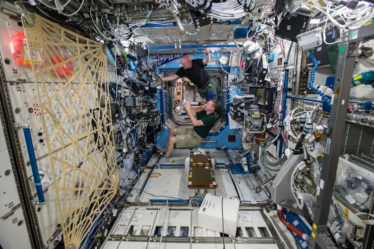 Two astronauts working with equipment in a room in the ISS.