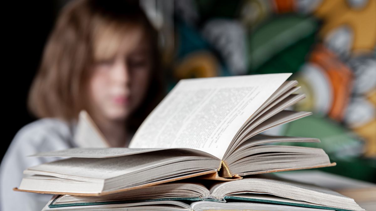 Dyslexia is hereditary: a stack of open books on a desk, featuring a blurred girl with a worried expression in the background. Photo: pvproductions / freepik.