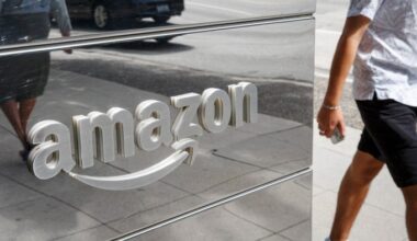 The Amazon logo on a reflective office wall, with pedestrians and street activity visible in the reflection.