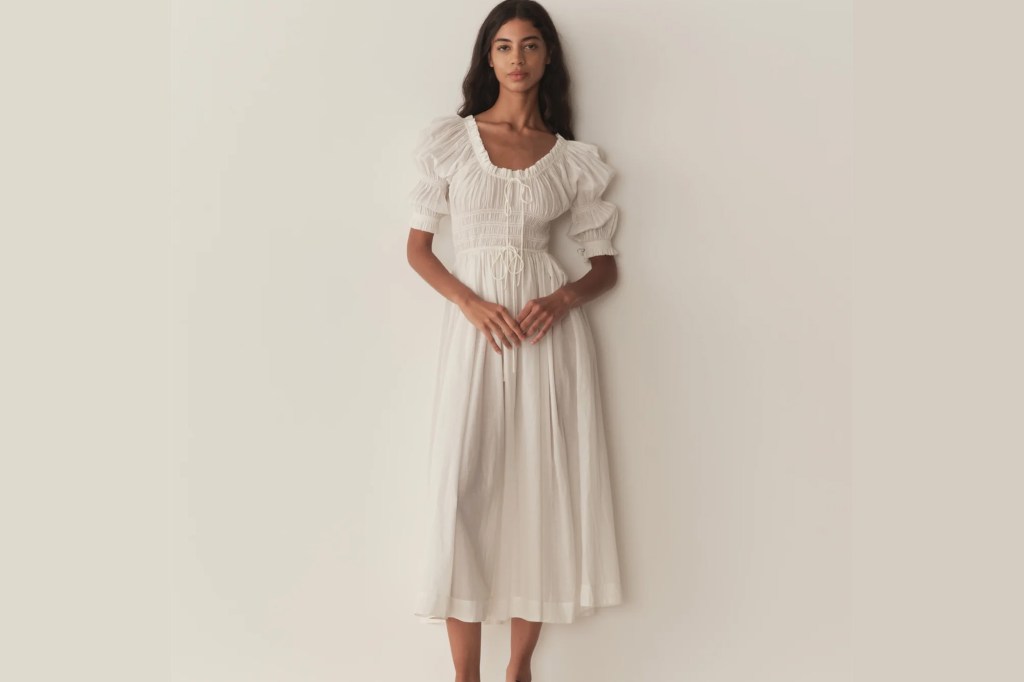A woman in a white, puff-sleeved midi dress with a square neckline and ties at the bust.