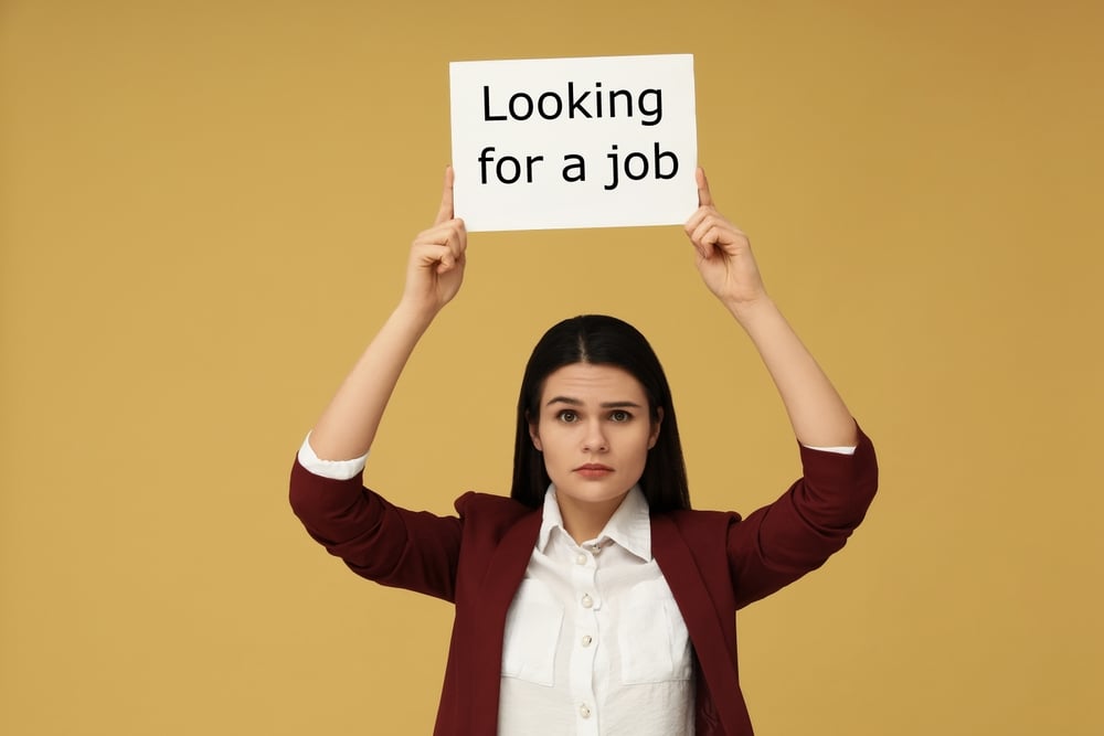 A young woman holds a sign that reads 'Looking for a job'