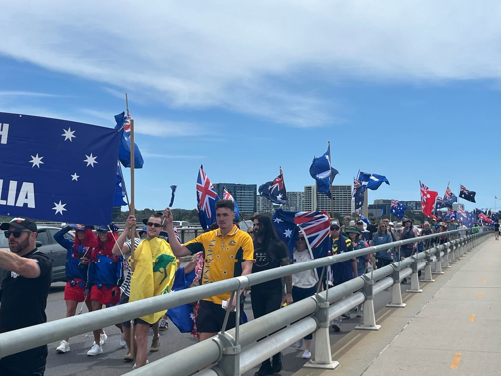 A group of people holding Australian flags marhcing across a bridge.