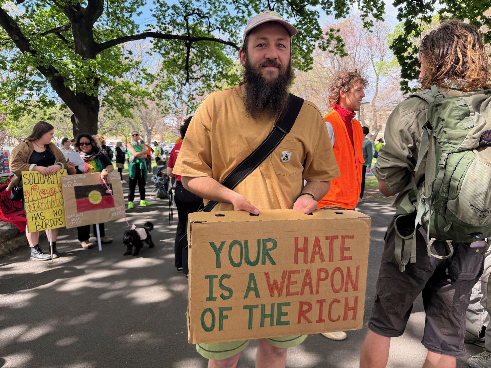Angus Dore stands with a cardboard sign that says, your hate is  a weapon of the rich
