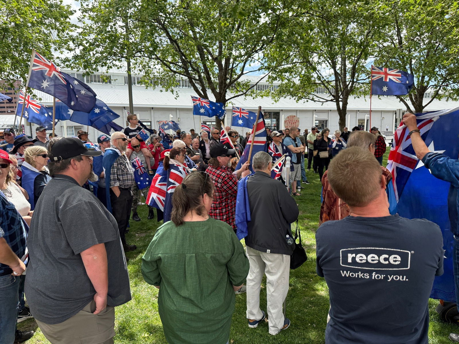 A crowd of people, some holding Australian flags, others wearing Australian flags as capes