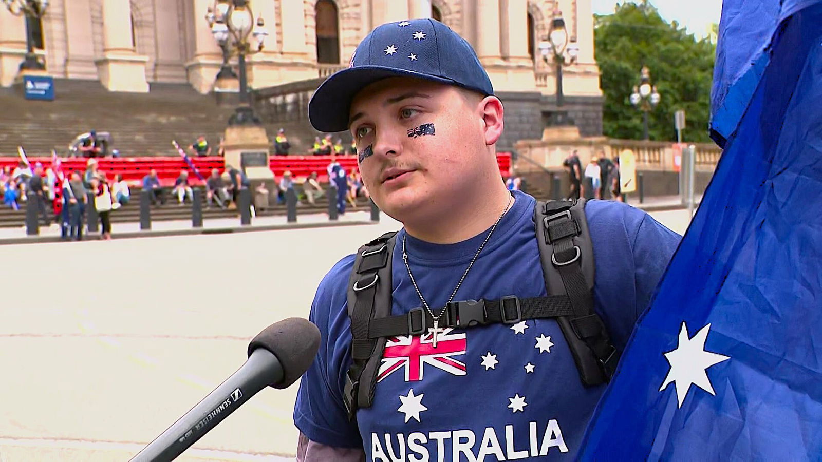 A man speaks into a microphone wearing a t shirt with an Australian flag on it