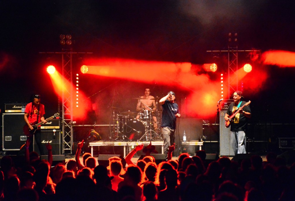 A punk band performs on a stage illuminated in red light.