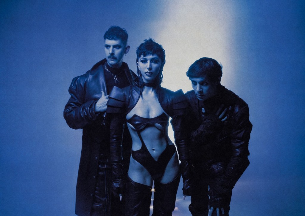 Three people dressed in leather pose in front of a blue background.