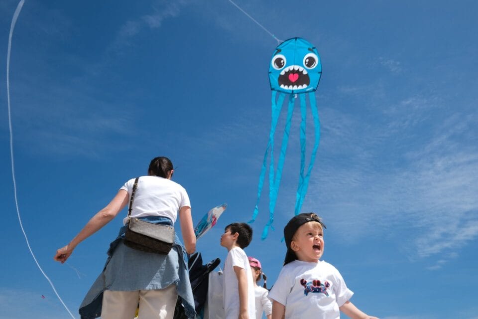 a kite with a cartoon character making a screaming face flies in the sky as a child on the ground below mimics the facial expression