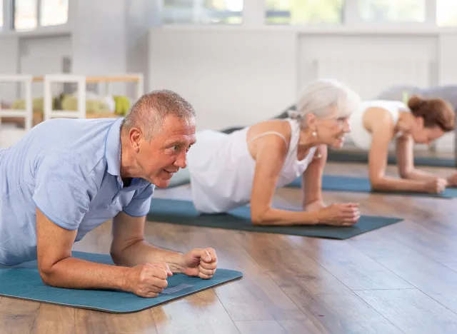 Active pensioners in sportswear performing plank exercise during group Pilates workout in fitness studio