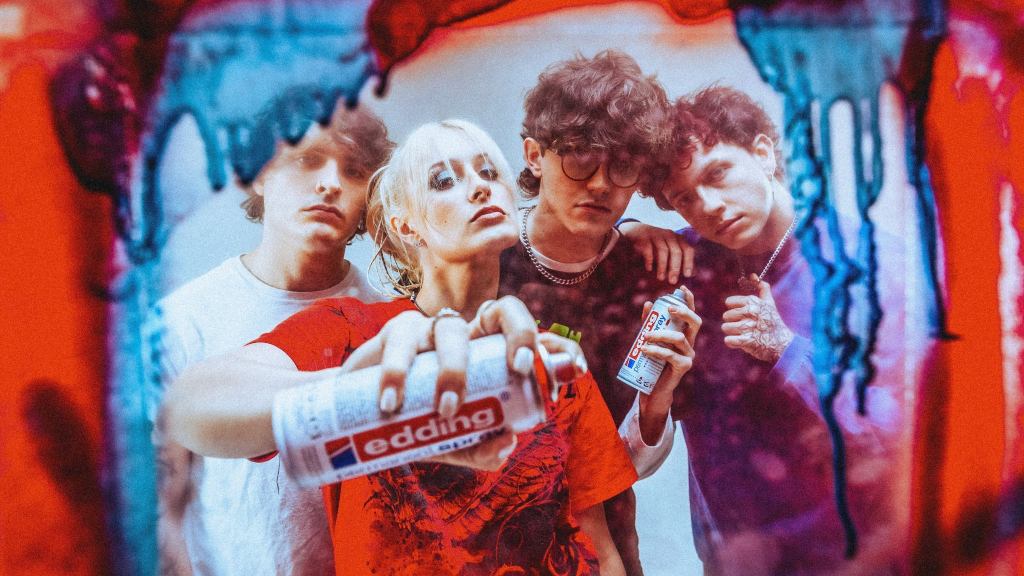 Four musicians standing together while one holds a spray paint can.