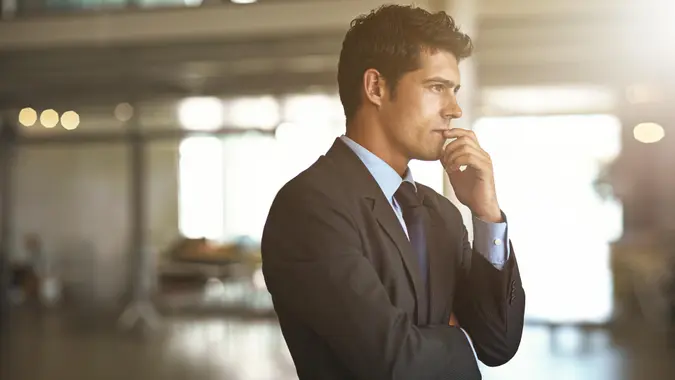 A successful businessman thinking while standing inside his company contemplating his wealth and money moves.