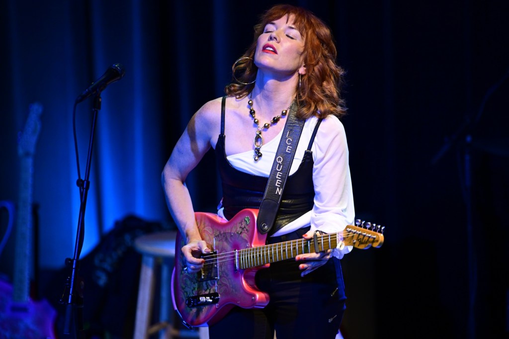 A red-haired woman plays an electric guitar passionately. 