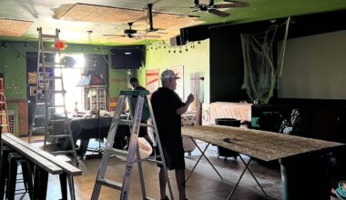 Two people conduct repair work amid ladders inside a bar,