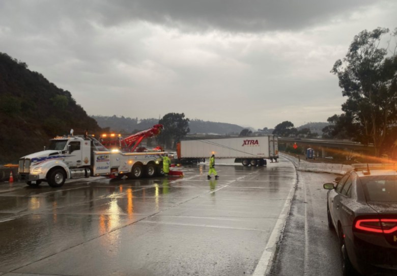 A truck sits on an empty freeway, wet from a storm, with a two truck nearby.