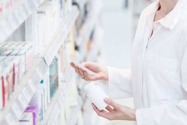 Female pharmacist reading prescription with pill bottle in one hand in pharmacy