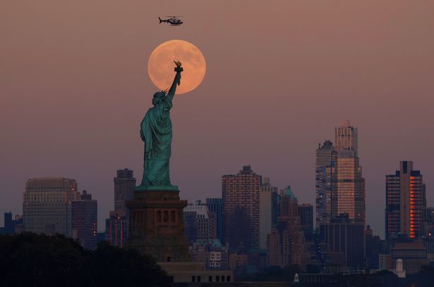 The Harvest Supermoon rises behind the Statue of Liberty and the Brooklyn skyline in New York City