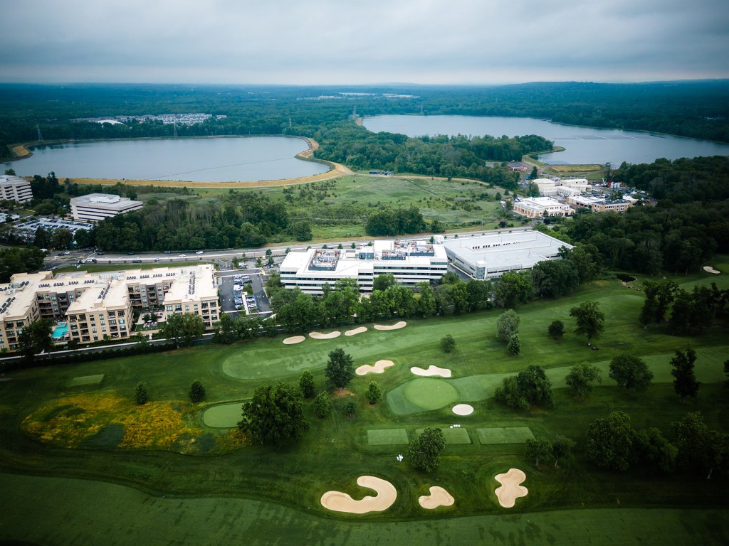 Aerial drone view of a golf course, residential buildings, commercial properties, and two lakes in Millburn, New Jersey.
