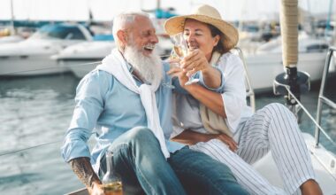 Senior couple toasting champagne on sailboat vacation - Happy elderly people having fun celebrating wedding anniversary on boat trip - Love relationship and travel lifestyle concept.
