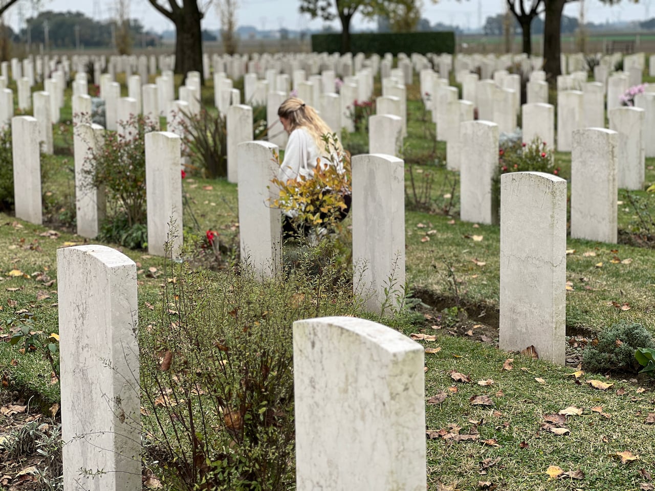 A young woman with blonde hair lays flowers at a war cemetery in Italy.