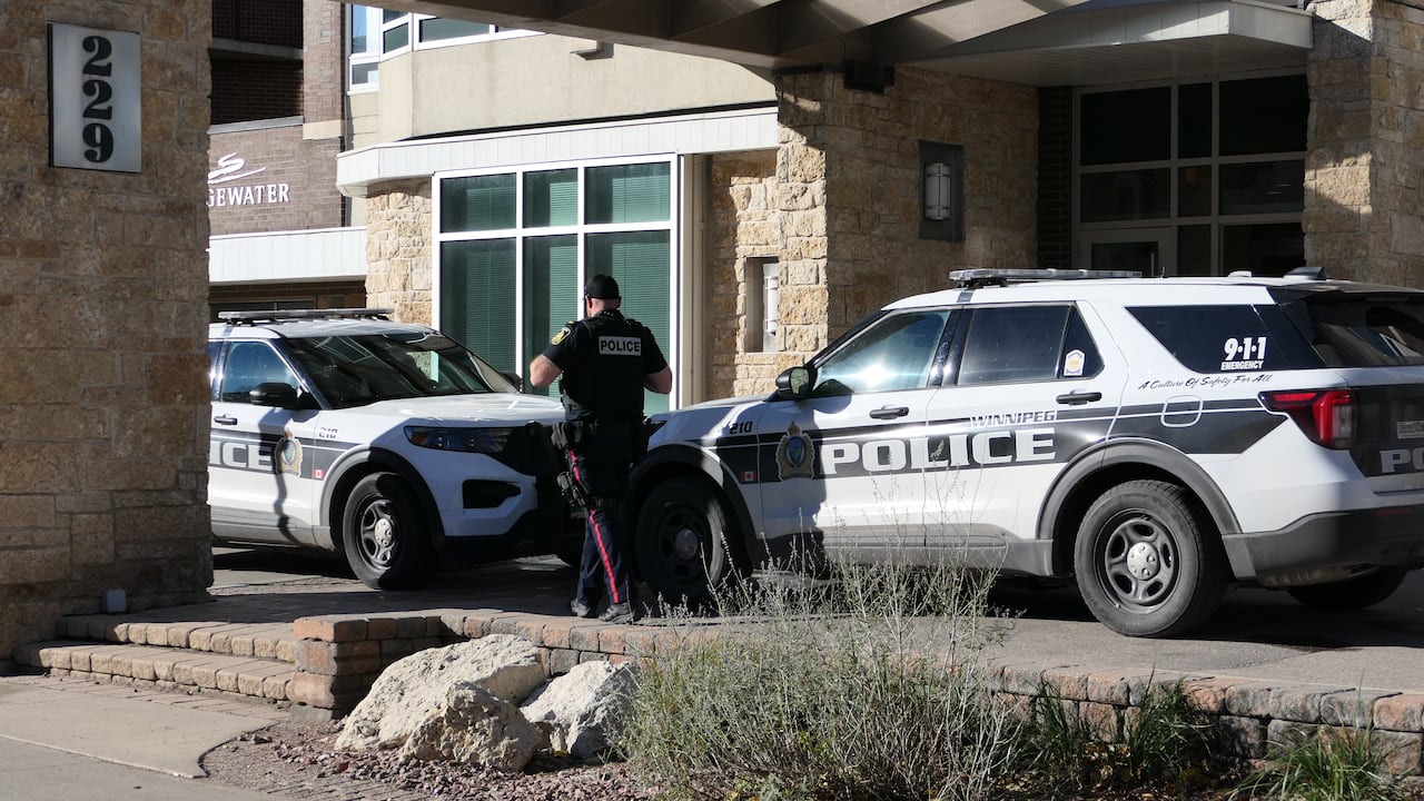 A police officers walks between two vehicles parked outside a residential building's entrance.